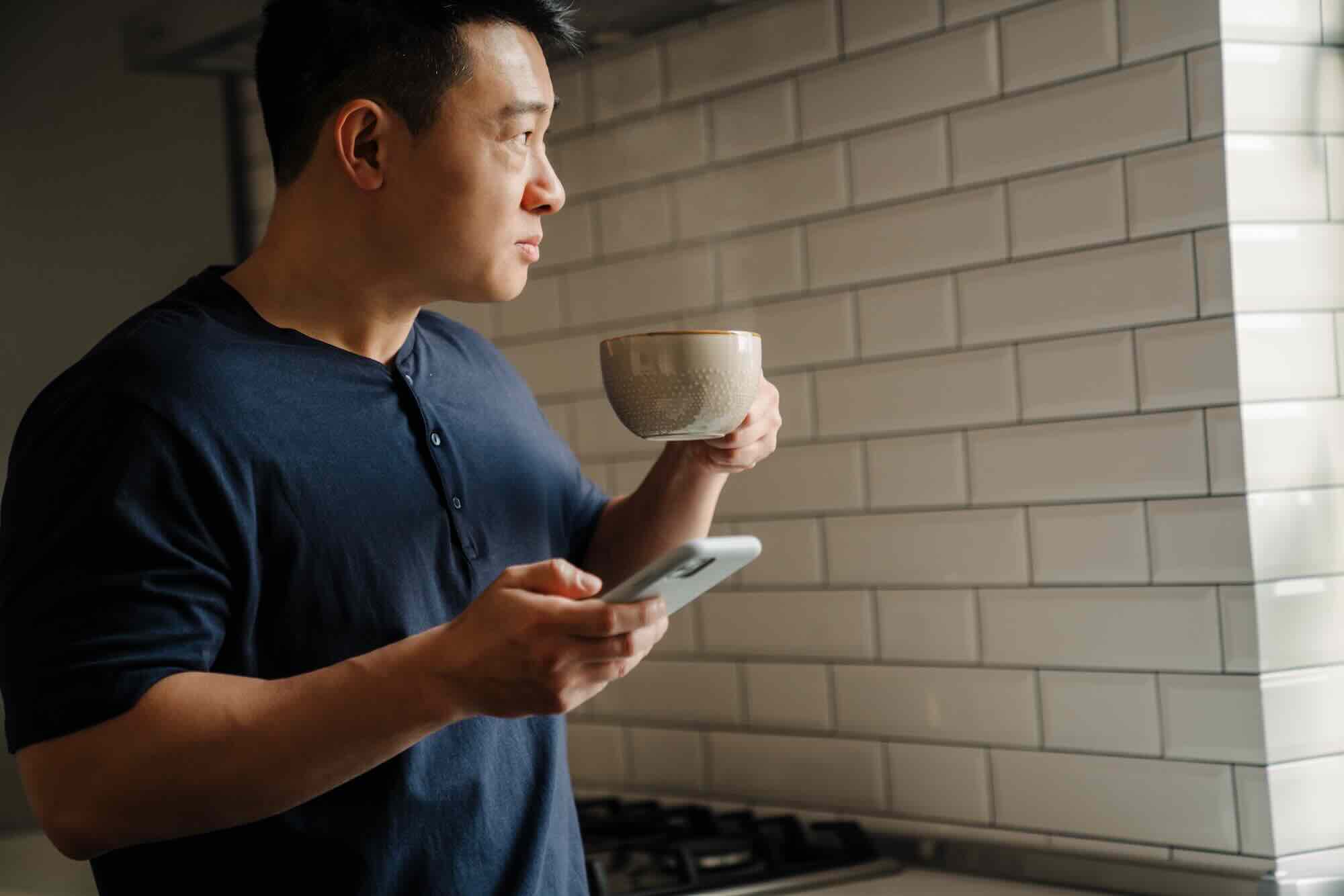 A man sits against a plain wall reading a message on his phone with a steady, unimpressed expression
