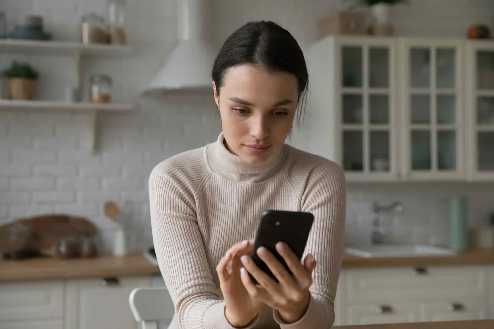 A person looking at their phone with a thoughtful, composed expression, choosing to pause before responding