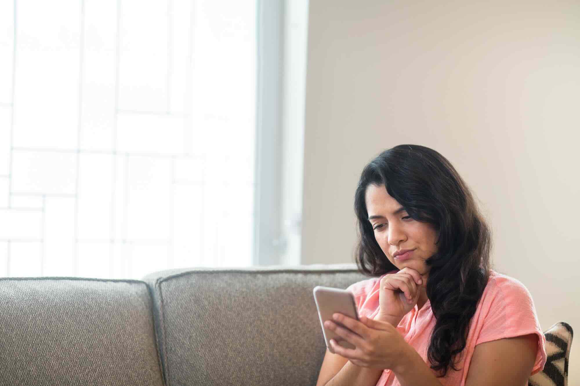 A parent sitting at a kitchen table looking at a phone with no reply, an unanswered message on the screen
